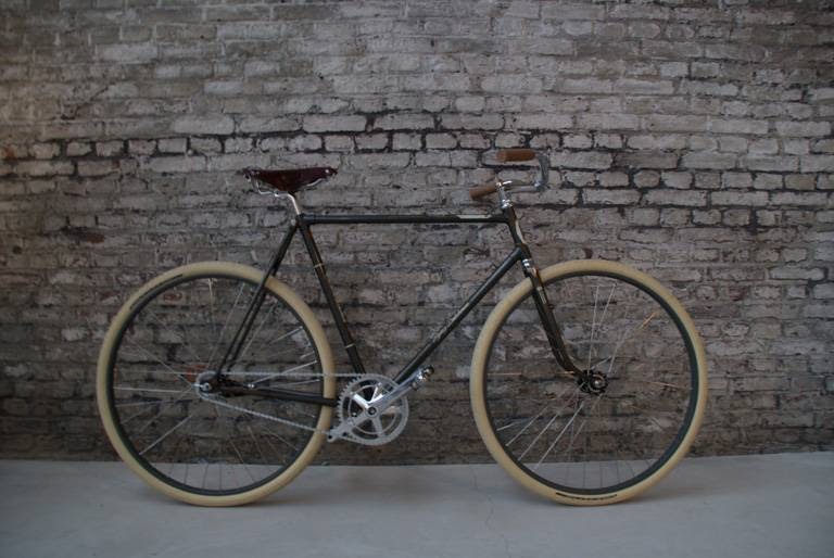 Een zwarte BRINKHAUS-fiets met crèmekleurige banden tegen een bakstenen muur